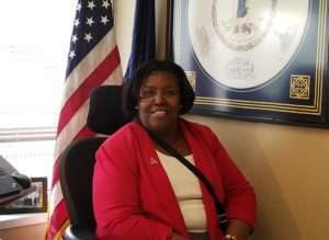 Karen Downing, an African American woman, sits at a desk with an American flag behind her.