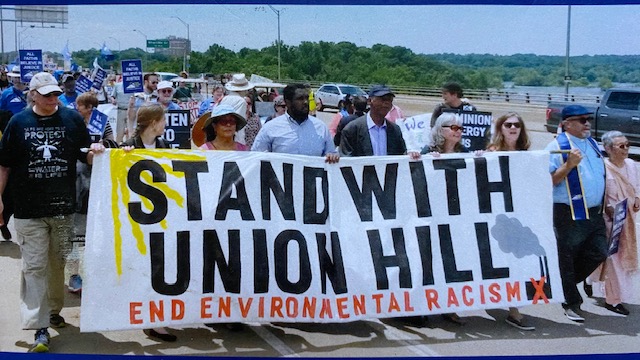 Picture: Members of Friends of Buckingham march in Richmond holding a banner that reads, "Stand with Union Hill - End Environmental Racism" in a big crowd.
