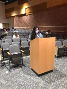 Picture of Cynthia Reyes in a mask standing at the podium at the school board meeting.