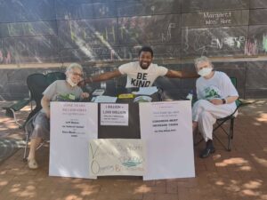 Three people sit behind a table in front of the Free Speech Wall in Charlottesville. Signs on the table advocate increasing taxes on the ultra-wealthy