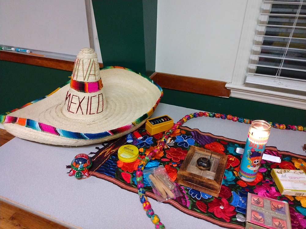 A table with colorful objects on a cloth, a candle, and a hat from Mexico