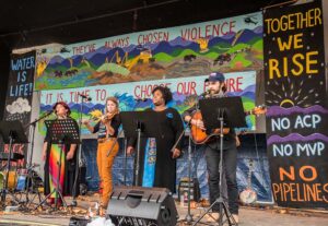 A picture of 4 musicians performing in front of NO MVP signs and art