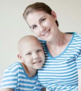 A woman and a child who is bald sit together and smile. Both wear blue and white striped shirts.