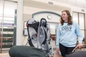 Woman with a Community Gear Library sweatshirt stands next to a backpack and bags in a library.